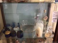 Overview of lot showing glass jars, crystal bowl, glass animals, and candles arranged in display cabinet