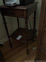 Front and side views of the antique ornate wooden end table showing turned legs, drawer with knob, and lower shelf.