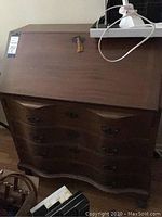 Front view of antique writing bureau secretary desk with closed drop-front and key in lock, showing curved drawer fronts and ornate handles.