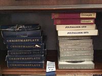 Various stacked boxes of blue Christmas plates from Porsgrund Norway including Jultallrik 1970 and 1971, Christmasplate '72 and '73, and multiple boxes labeled CHRISTMASPLATE