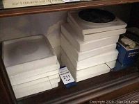 Stacked white plates stored on shelf with visible blue painted designs on top plates.