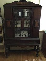 Front view of the large solid wood display cabinet showing carved panels, metal grille on glass door, and drawer below.