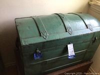 Full view of green metal dome-top trunk with domed lid, metal reinforcements, and lock on front.