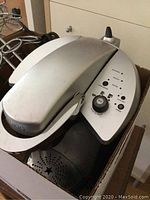 Silver Keurig coffee maker with oval shape and control buttons visible on top surface.