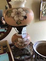 Full view of lamp showing floral painted designs on peach colored glass and metal base.
