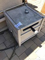 Outdoor hose reel box sitting on patio floor with closed lid and garden hose attached to side.