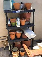 Full view of black plastic shelving unit with assorted plant pots and gardening items on each shelf.