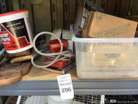 Photo showing red electric hand sander with cord, plaster of Paris bucket, plastic storage container holding several boxes including Perko box