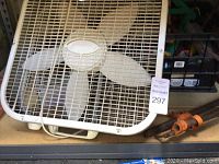 White box fan seen on shelf with part of lot visible in background.
