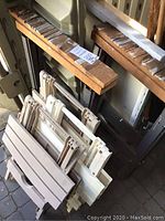 Photo showing stacked beige plastic folding tables and wooden workhorses with noticeable wear and paint marks.