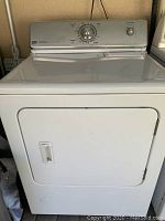Front view of white Maytag gas dryer showing door, control panel with knob and start button, some rust visible on door hinges.