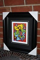 Framed and matted artwork with corner protectors on black frame against brick wall.