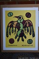 Full view of "Thunderbird" print by Norval Morrisseau showing stylized bird figure with colored orbs on yellow background mounted on cardboard.