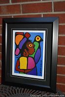 View of framed "Shaman with Bird" print showing the full artwork and frame against a brick wall.