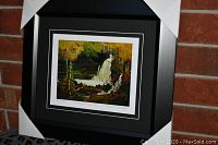 Framed artwork showing a black matted frame with a colorful waterfall scene print inside with protective corner guards still on the frame.