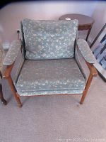 Front view of teak lounge chair with loose seat and back cushions covered in light blue floral fabric