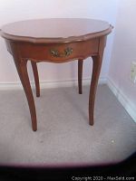 Front view of vintage tall wooden end table showing decorative drawer handle and curved legs.