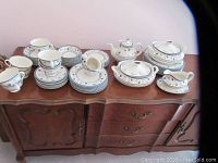 Full lot of Royal Doulton Cambridge pattern bone china on a wooden cabinet showing all groupings including plates, cups, sugar bowl, teapot, and serving dishes.