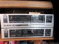 Photo showing JVC KD-V300 stereo cassette deck on a shelf beneath the JVC R-K200 stereo receiver, featuring cassette slot, tape select switch, and LED peak indicators.