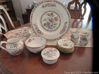 Display of all china items in the lot including large plate, small plates, cups, bowls, and covered dish on wooden table