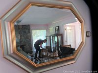Framed octagonal wall mirror hanging on wall reflecting room interior.