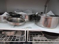 Shelf with various vintage pots and pans including saucepans and stockpot with lids and frying pans, showing wear and use.