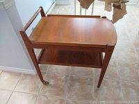 Side view of the two-tier wooden bar cart on tiled floor.