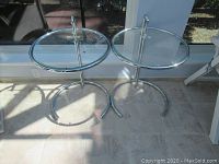 Front view of both round glass-top side tables on chrome-plated metal frames.