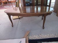 Angled photo showing full mahogany coffee table with oval top and carved legs on carpeted floor
