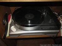 Photo showing ION record player with vinyl record on platter. Dust cover closed and light wear visible on the unit.