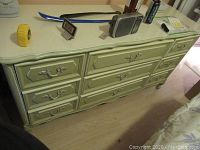 Front and top side view of French Provincial style dresser showing nine drawers and ornate handles with decorative drawer front panels.