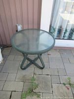 Patio side table with round textured glass top and green metal tubular base, photographed on outdoor patio stone tiles from higher angle