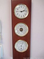 Full view of wooden wall clock with three dials: clock, barometer, and thermometer/hygrometer.
