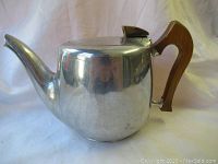 Side view of Picquot Ware teapot showing metal body, curved spout, and wooden handle.