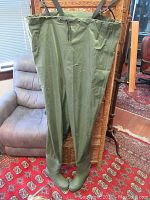 Full view of the green fishing waders displayed hanging with attached boots visible.