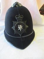 Front view of black felt policeman's helmet with metal badge and crown emblem.