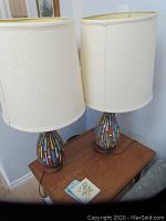 Pair of mid-century modern table lamps with colorful mosaic bases and tall off-white fabric shades on wooden table