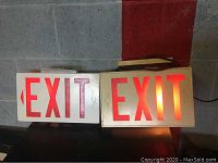 Both EXIT signs side by side, one illuminated red, both with power cords visible