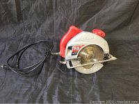 Red and silver SkilSaw circular saw with power cord. Shows the full side and part of the blade.