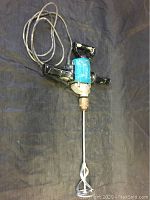 Full view of the Makita power tool with the long mixing attachment on a black surface.