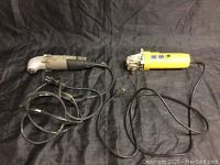 Two corded electric power tools lay flat on a dark surface, one is the Rockwell right angle drill and the other is the yellow Power Fist angle grinder.
