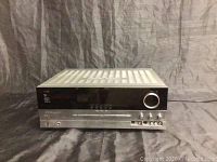 Front view of the Harman Kardon receiver showing its control panel, large volume knob, buttons, and RCA input/output ports.