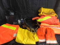 Photo showing the tool belt, various safety clothing, gloves, and the protective mask and glasses laid out against black background.