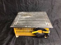 Top-side view of the portable table saw showing the metal top surface with the circular saw blade recessed in the center and the yellow metal base below.