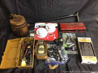 Wide view of all lot items including wooden keg, Cain display bottle, fishing spool, smoke alarms, and various tools and hardware