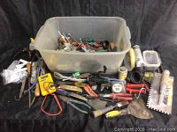Overview of plastic bin with various hand and measuring tools scattered outside on black cloth