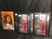 Four black 11x17 inch picture frames with placeholder images showing a red British telephone booth in a cityscape, arranged side by side with Bob Marley plaque partially visible on left side.