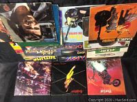 Top view of a stack of assorted vinyl records showing album covers including a portrait of a man, guitars, and colorful graphics.