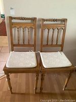 Two wooden dining chairs with rattan seats and padded cushions viewed from front.