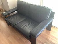 Front view of black Scandinavian leather love seat showing seat cushions, armrests, and wooden legs.